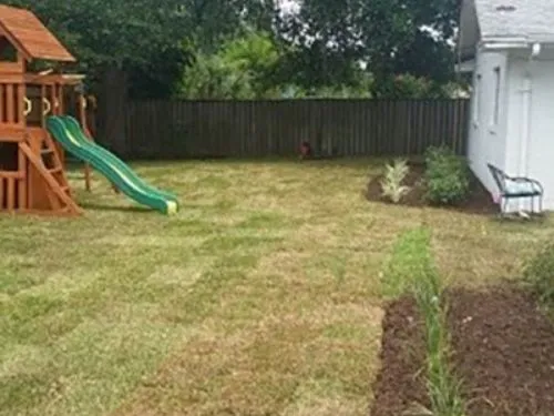 New sod in a fenced backyard with a wooden playset