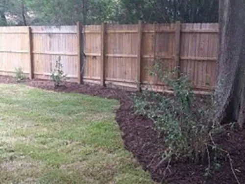 Sod lawn meeting a mulched bed along a wood privacy fence
